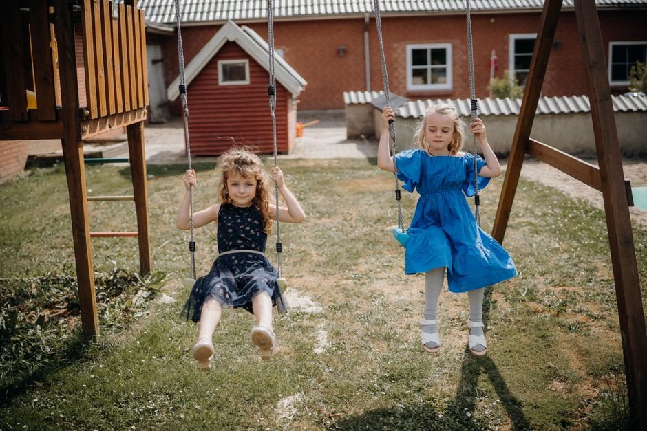 Dvi mergaitės linksminasi supynėse saulėtoje aikštelėje, pabrėžiant ilgaamžiškumą