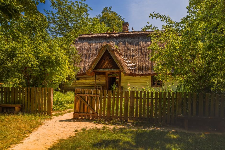 Kaimo namas šiaudiniu stogu, apsuptas žalumos. Pavyzdys, kaip derinti namelius kieme