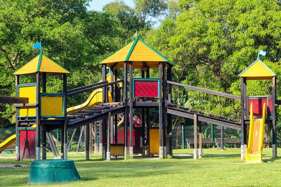 Spalvinga žaidimų aikštelė saulėtame parke, kur darniai dera žalia gamta ir vaikų erdvė